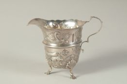 AN IRISH STYLE SILVER CREAM JUG repousse decoration on three claw feet. Birmingham 1912.