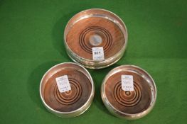 A silver wine bottle coaster and pair of similar coasters.