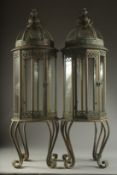 A LARGE PAIR OF METAL GLAZED LANTERNS on four curving legs. 33ins high.
