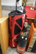 A large empty champagne bottle and a part set of golf clubs with bag.