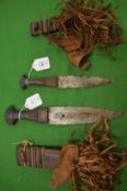 Two African daggers with decorative leather handles and scabbards.