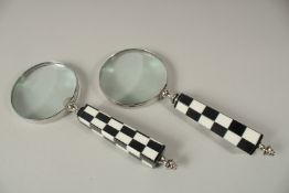 A PAIR OF MAGNIFYING GLASSES with black and white chequered handles.