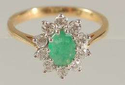 AN 18CT YELLOW AND WHITE GOLD OVAL EMERALD AND RBC DIAMOND CLUSTER RING. Emerald 0.80ct. Diamonds