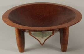A VERY LARGE FIJIAN KAVA CARVED HARDWOOD BOWL, raised on four legs, with mounted metal plaque