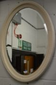 A white painted oval wall mirror.