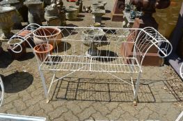 A white painted wrought iron and wire work scroll-end garden bench.