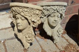 A pair of reconstituted stone wall brackets modelled as female faces.