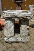 An unusual large square shaped bird bath on four column supports with slab base.