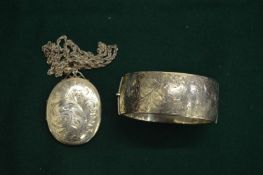 A silver bangle and a large silver locket with engraved decoration.