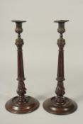 A PAIR OF GEORGIAN STYLE MAHOGANY WOODEN CANDLESTICKS with cast metal sconces, on circular bases.