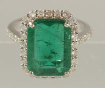AN 18ct WHITE GOLD LARGE EMERALD-CUT EMERALD AND RBC DIAMOND CLUSTER RING with diamond shoulders.