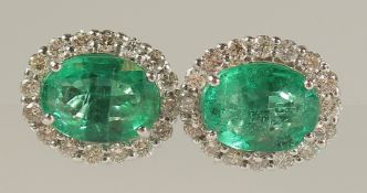 A PAIR OF 18ct WHITE GOLD OVAL EMERALD AND RBC DIAMOND CLUSTER STUDS, boxed. Emeralds 3.17ct.