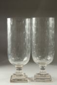 A PAIR OF GLASS STORM LANTERNS on square stepped bases. 36cms high.