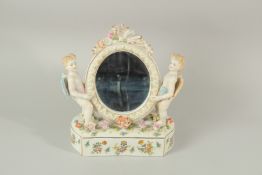 A CONTINENTAL PORCELAIN OVAL MIRROR with cupid supports and encrusted with flowers. 27cms high.