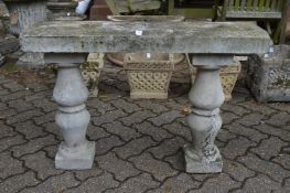 A reconstituted stone garden seat with pedestal supports.