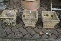 A set of three reconstituted stone square shaped garden planters.