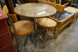 A small circular granite top kitchen table with chrome support together with a pair of chairs.
