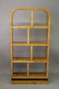 AN ART DECO DESIGN BLOND WOOD DISPLAY UNIT with a curving top and an arrangement of eight open