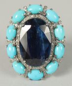 A LARGE OVAL CLUSTER RING IN WHITE METAL SET WITH A LARGE OVAL KYANITE SURROUNDED BY TURQUOISE AND