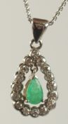 A 9CT WHITE GOLD EMERALD AND DIAMOND PENDANT on a chain.