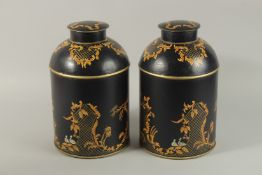 A PAIR OF BLACK TOLEWARE CIRCULAR CANNISTERS AND COVERS. 34cm high.