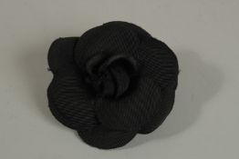 A CHANEL BLACK FABRIC FLOWER BROOCH. 10cm diameter in a Chanel box.