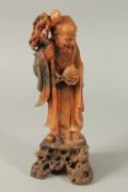 A FINELY CARVED CHINESE CORAL-RED SOAPSTONE FIGURE OF SHOU LAO, raised upon a rocky mound, 30cm