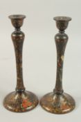 A PAIR OF PERSIAN QAJAR LACQUERED WOOD CANDLESTICKS, decorated with figures and flora, 26.5cm high.