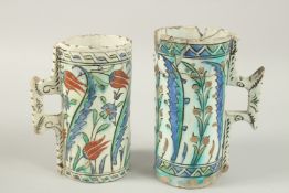 TWO EARLY IZNIK GLAZED POTTERY TANKARDS, each painted with foliate decoration, largest 20cm high.