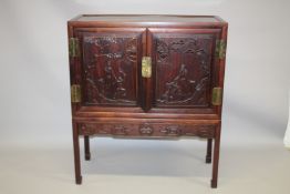 A CHINESE REDWOOD SIDE CABINET, 20TH CENTURY, the pair of doors carved with figures in a