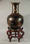 A LARGE JAPANESE GILDED BLACK LACQUERED VASE ON HARDWOOD STAND, the vase painted with panels of