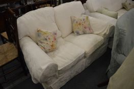 A small two seater cream upholstered settee.
