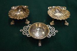 Two shell shaped salts and a tea strainer.