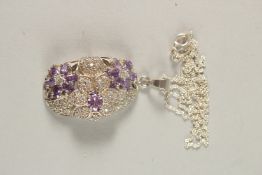 A DECORATIVE SILVER PENDANT AND CHAIN set with purple stones in a flowerhead design.