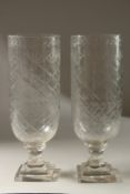A PAIR OF GLASS STORM LANTERNS on square stepped bases. 34cms high.