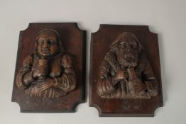 A PAIR OF GERMAN CARVED WOOD PLAQUES, a man and a woman holding wine cups. 35cms x 24cms.