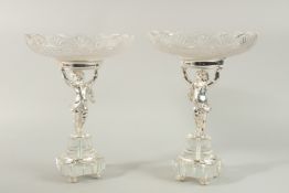 A GOOD PAIR OF SILVER PLATED CUPID COMPORTS with cut glass dishes. 33cms high.