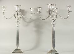 A LARGE PAIR OF SILVER PLATED FOUR BRANCH CANDELABRA with column support on a square base.