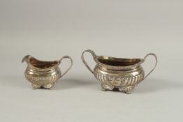 A GEORGE III TWO HANDLED SUGAR BASIN AND MILK JUG on claw feet. London 1819, weight: 16ozs.