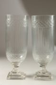 A PAIR OF GLASS STORM LANTERNS on square stepped bases. 34cms high.