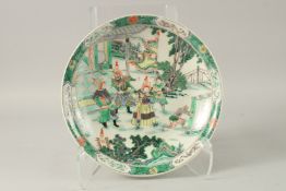 A CHINESE FAMILLE VERTE PORCELAIN PLATE, painted with figures in a courtyard, the base with symbol