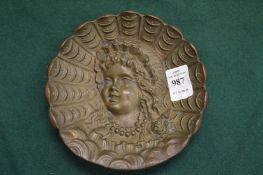 A cast metal dish depicting the bust of a woman.