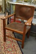 An Arts and Crafts walnut framed armchair with leather upholstered back and seat.