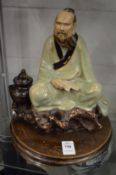 A Chinese pottery model of a sage seated on a rock.