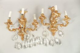 A PAIR OF GILT METAL THREE LIGHT WALL SCONCES with cut glass prism drops. 35cms high.