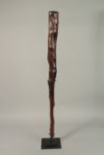 A CARVED WOOD CLUB. 100cms high, on a metal stand.