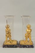 A GOOD PAIR OF GILT BRONZE AND GLASS VASES with gilt cupids on a Blue John base. 24cms high.