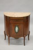 A HALF MOON SIDE CUPBOARD with marble top, panel door to the front with Wedgwood oval plaque.