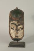 A CARVED WOOD AND PAINTED MASK. 16cms x 15cms on a metal stand.