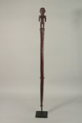 A CARVED WOOD CLUB, the handle as a standing female. 99cms high, on a metal stand.